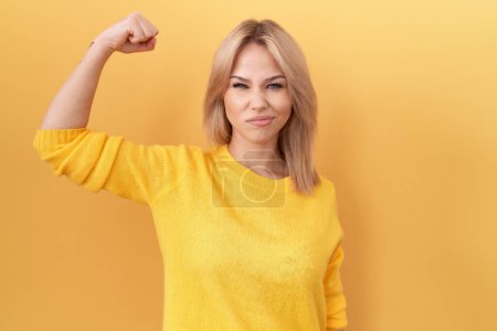 Foto de Mujer joven caucásica usando suéter amarillo fuerte persona mostrando el músculo del brazo, confiado y orgulloso de poder - Imagen libre de derechos