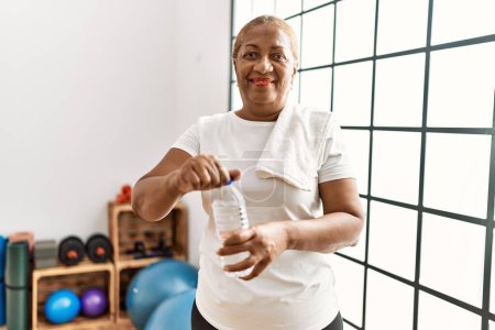 Téléchargez les photos : Femme afro-américaine âgée souriante eau potable confiante au centre sportif - en image libre de droit