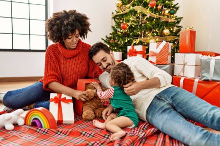 Photo for Couple and daughter playing with toys sitting by christmas tree at home - Royalty Free Image