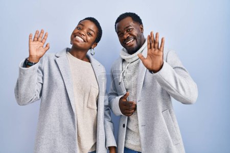 Téléchargez les photos : Jeune couple afro-américain debout sur fond bleu ensemble renonçant à dire bonjour heureux et souriant, geste de bienvenue amical - en image libre de droit