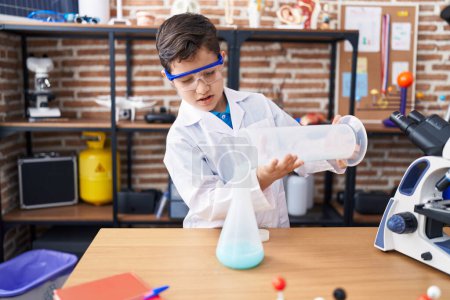 Foto de Adorable niño hispano estudiante vertiendo líquido en tubo de ensayo en el aula de laboratorio - Imagen libre de derechos