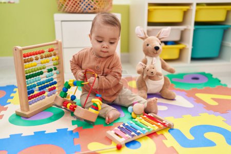 Foto de Adorable niño hispano jugando con juguetes sentados en el suelo en el jardín de infantes - Imagen libre de derechos