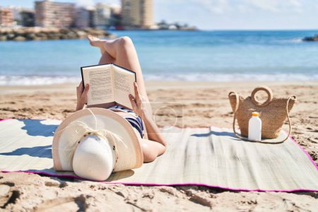 Téléchargez les photos : Jeune femme hispanique portant bikini et chapeau d'été livre de lecture au bord de la mer - en image libre de droit