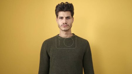 Photo for Young hispanic man standing with serious expression over isolated yellow background - Royalty Free Image