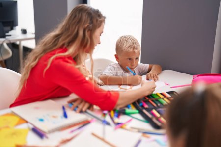 Foto de Profesor y niño pequeño sentados en la mesa dibujando sobre papel en el aula - Imagen libre de derechos