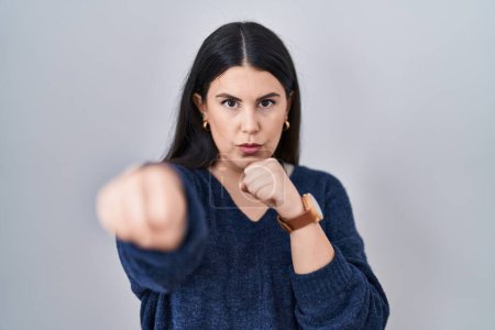 Téléchargez les photos : Jeune femme brune debout sur fond isolé coups de poing poing pour se battre, agressif et en colère attaque, menace et violence - en image libre de droit