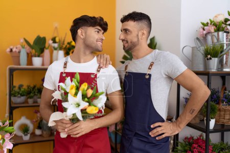 Téléchargez les photos : Two hispanic men florists smiling confident holding bouquet of flowers at flower shop - en image libre de droit