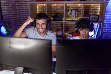Téléchargez les photos : Two hispanic men streamers playing video game with winner expression at gaming room - en image libre de droit