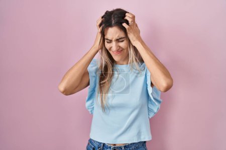 Photo for Young hispanic woman standing over pink background suffering from headache desperate and stressed because pain and migraine. hands on head. - Royalty Free Image