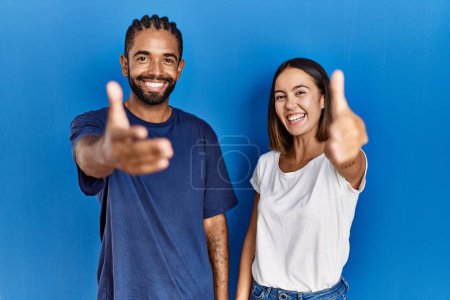 Foto de Joven pareja hispana de pie juntos sonriendo amistoso ofreciendo apretón de manos como saludo y bienvenida. negocios exitosos. - Imagen libre de derechos