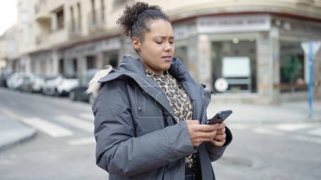 Photo for African american woman using smartphone with serious expression at street - Royalty Free Image