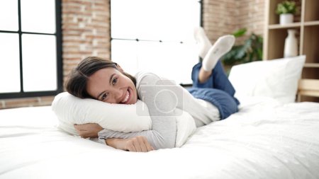 Téléchargez les photos : Jeune belle femme hispanique étreignant oreiller couché sur le lit dans la chambre - en image libre de droit
