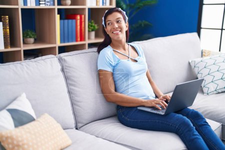 Téléchargez les photos : Jeune belle femme hispanique utilisant un ordinateur portable assis sur le canapé à la maison - en image libre de droit