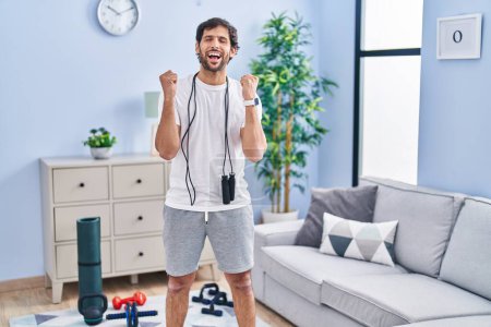 Photo for Handsome latin man wearing sportswear at home celebrating mad and crazy for success with arms raised and closed eyes screaming excited. winner concept - Royalty Free Image