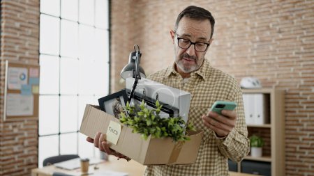 Foto de Hombre de mediana edad trabajador de negocios despedido celebración de la caja de cartón utilizando el teléfono inteligente en la oficina - Imagen libre de derechos