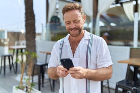 Téléchargez les photos : Middle age man smiling confident using smartphone at coffee shop terrace - en image libre de droit