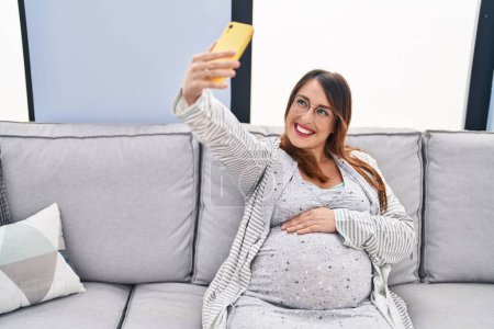 Téléchargez les photos : Young pregnant woman make selfie by smartphone sitting on sofa at home - en image libre de droit