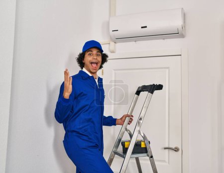 Photo for Hispanic man with curly hair working at home renovation celebrating victory with happy smile and winner expression with raised hands - Royalty Free Image