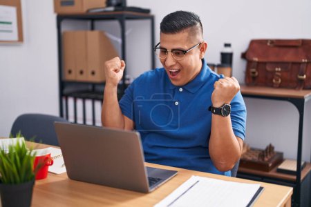 Photo for Young hispanic man working at the office with laptop celebrating surprised and amazed for success with arms raised and open eyes. winner concept. - Royalty Free Image