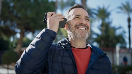 Photo for Middle age man smiling confident listening voice message by the smartphone at park - Royalty Free Image