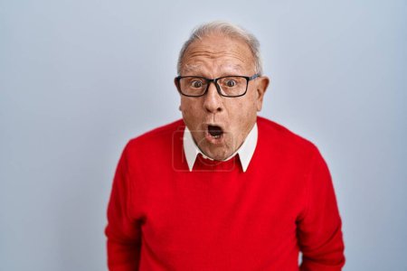 Foto de Hombre mayor con el pelo gris de pie sobre el fondo aislado en la cara de choque, con aspecto escéptico y sarcástico, sorprendido con la boca abierta - Imagen libre de derechos