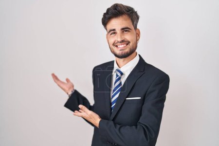 Foto de Joven hombre hispano con tatuajes con traje de negocios y corbata invitando a entrar sonriente natural con la mano abierta - Imagen libre de derechos
