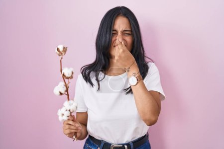 Photo for Brunette woman standing over pink background smelling something stinky and disgusting, intolerable smell, holding breath with fingers on nose. bad smell - Royalty Free Image