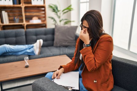 Photo for Young hispanic woman working as psychology counselor tired rubbing nose and eyes feeling fatigue and headache. stress and frustration concept. - Royalty Free Image
