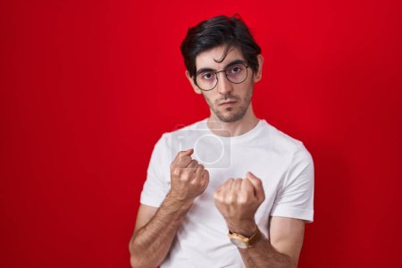 Téléchargez les photos : Young hispanic man standing over red background ready to fight with fist defense gesture, angry and upset face, afraid of problem - en image libre de droit