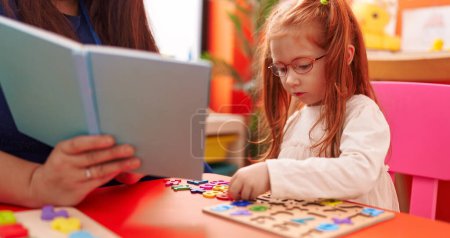 Foto de Adorable chica pelirroja jugando con matemáticas juego de puzzle sentado en la mesa en el jardín de infantes - Imagen libre de derechos