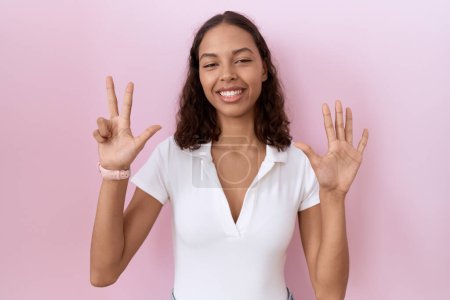 Photo for Young hispanic woman wearing casual white t shirt showing and pointing up with fingers number eight while smiling confident and happy. - Royalty Free Image
