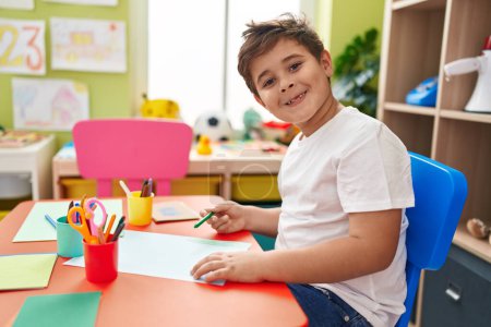 Téléchargez les photos : Adorable hispanic boy preschool student sitting on table drawing on paper at kindergarten - en image libre de droit