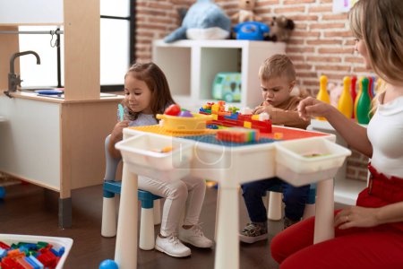 Foto de Profesor con niño y niña jugando con bloques de construcción sentados en la mesa en el jardín de infantes - Imagen libre de derechos