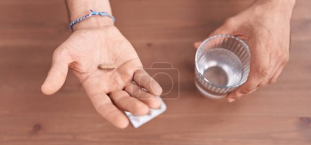 Téléchargez les photos : Jeune homme hispanique tenant pilule et verre d'eau à la maison - en image libre de droit