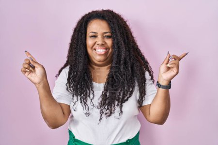 Téléchargez les photos : Plus taille hispanique femme debout sur fond rose souriant confiant pointant avec les doigts vers différentes directions. espace de copie pour la publicité - en image libre de droit