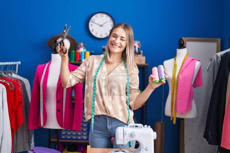 Téléchargez les photos : Young caucasian woman tailor smiling confident holding scissors and thread at sewing studio - en image libre de droit