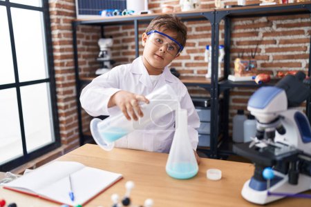 Téléchargez les photos : Adorable hispanic boy student pouring liquid on test tube at laboratory classroom - en image libre de droit
