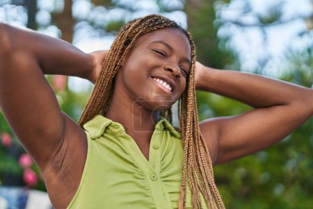 Foto de African american woman smiling confident relaxed with hands on head at park - Imagen libre de derechos