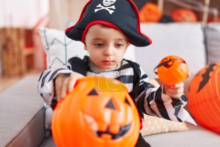 Foto de Adorable chico hispano teniendo fiesta de halloween sosteniendo canasta de calabaza en casa - Imagen libre de derechos