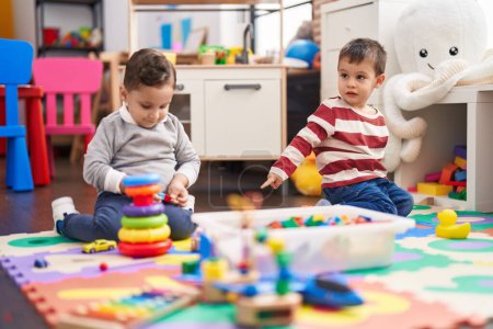 Foto de Two kids playing with toys sitting on floor at kindergarten - Imagen libre de derechos