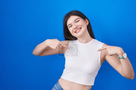 Photo for Young caucasian woman standing over blue background looking confident with smile on face, pointing oneself with fingers proud and happy. - Royalty Free Image
