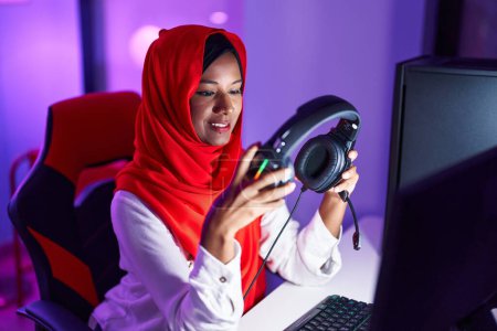 Téléchargez les photos : Young beautiful woman streamer smiling confident holding headphones at gaming room - en image libre de droit