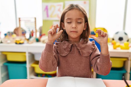 Téléchargez les photos : Adorable hispanic girl preschool student sitting on table crossing fingers at kindergarten - en image libre de droit