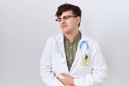 Photo for Young non binary man wearing doctor uniform and stethoscope with hand on stomach because nausea, painful disease feeling unwell. ache concept. - Royalty Free Image