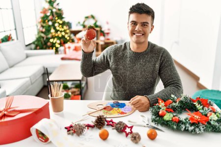 Photo for Young hispanic man holding christmas ball decoration at home - Royalty Free Image