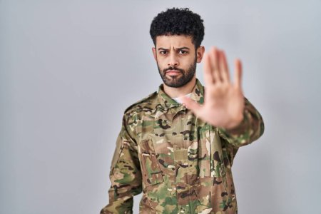 Téléchargez les photos : Un Arabe portant un uniforme de camouflage de l'armée arrête de chanter avec la paume de la main. expression d'avertissement avec geste négatif et sérieux sur le visage. - en image libre de droit