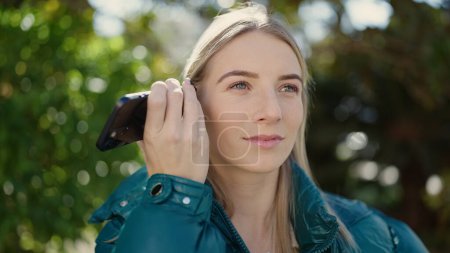 Photo for Young blonde woman listening to voice message at park - Royalty Free Image