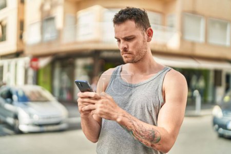 Téléchargez les photos : Jeune homme hispanique utilisant un smartphone avec une expression sérieuse dans la rue - en image libre de droit