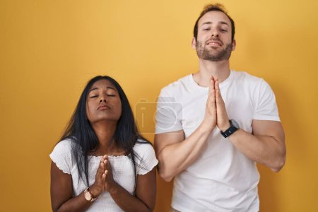 Photo for Interracial couple standing over yellow background begging and praying with hands together with hope expression on face very emotional and worried. begging. - Royalty Free Image