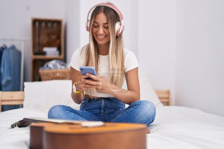 Photo for Young beautiful hispanic woman listening to music sitting on bed at bedroom - Royalty Free Image